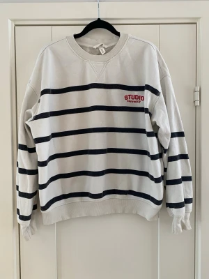 Randig sweatshirt från H&M strl M - Säljer en vit sweatshirt med svarta horisontella ränder från H&My. Tröjan har rund halsringning, ribbade muddar och tryckt logga i rött på bröstet. Tillverkad i mjuk bomullsmix, perfekt för en avslappnad och trendig look.Tröjan är lite nopprig och de svarta ränderna har bleknats lite i övrigt i bra begagnat skick.  Mått  Över bröstet: ca 69 cm Längd från axeln och ner: ca 61 cm  60% bomull och 40% polyester   Kommer från ett djur och rökfritt hem