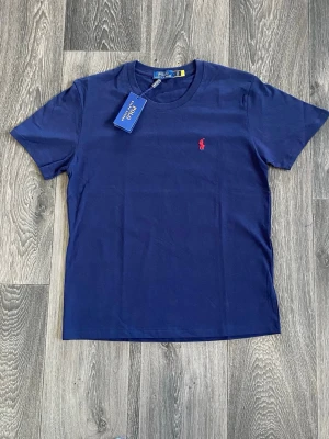 Marinblå t-shirt från Polo Ralph Lauren - Snygg marinblå t-shirt från Polo Ralph Lauren med klassisk röd logga broderad på bröstet. T-shirten har rund halsringning och korta ärmar. Tillverkad i mjuk bomull för skön känsla och stilren look.