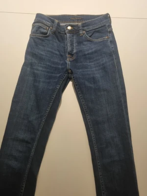 Nudie jeans w28 L32 - Snygga blå jeans från Nudie med klassisk femficksdesign och orangea sömmar på bakfickorna. Jeansen har normal passform och raka ben.
