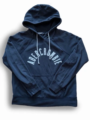 Mörkblå hoodie från Abercrombie - Mörkblå hoodie från Abercrombie med stor vit logga broderad över bröstet. Storlek L sitter mer som en S eller en liten M Skick 7/10, Pris är såklart diskuterbart!