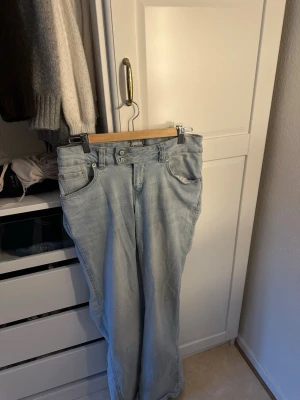 Ljusblå bootcut jeans med dubbla knappar - Säljer ett par ljusblå bootcut jeans med dubbla knappar i midjan från lager 157. Jeansen har en avslappnad passform och är tillverkade i mjukt denimtyg. Perfekta ny inför våren, för en trendig look. Jeansen är storlek 38, kom privat för fler bilder ❤️