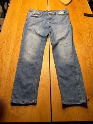 Blå raka jeans med slitningar - Säljer ett par klassiska blå jeans med raka ben och lätt slitna detaljer. Jeansen har fem fickor, normal midja och dragkedjegylf. Perfekta för en avslappnad och trendig look.
