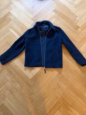 Mörkblå jacka med dragkedja - Stilren mörkblå jacka med hel dragkedja framtill och två fickor. Jackan har klassisk krage och raka ärmar, perfekt för en clean look. Materialet känns mjukt och passar bra till vardagsoutfits.