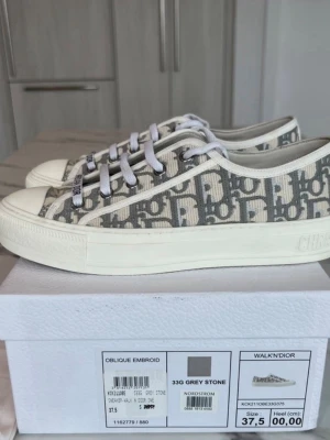 Dior Walk'n'Dior Oblique sneakers - Snygga Walk'n'Dior sneakers i canvas med grått och vitt Dior Oblique-mönster. Klassisk låg modell med vita snören och gummisula. Perfekta för dig som vill ha en lyxig och trendig look med tydlig logga och stilren design.