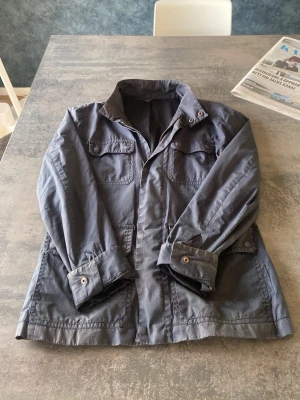 Field jacket - Snygg mörkgrå utilityjacka med fyra stora fickor framtill och knappar vid ärmsluten. Jackan har en rak passform och klassisk krage, perfekt för lager-på-lager. Materialet känns slitstarkt och jackan har en stilren, minimalistisk look.