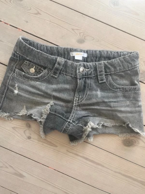 Grå jeansshorts från Gina Tricot - Snygga grå jeansshorts från Gina Tricot med slitna detaljer och råa kanter. Klassisk femficksmodell med knapp och dragkedja framtill. Perfekta för en avslappnad och cool stil.