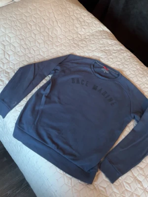 Blå sweatshirt från Race Marine - Mysig blå sweatshirt från Race Marine med rund halsringning och tryckt logga på bröstet. Tröjan har långa ärmar och ribbade muddar vid ärmslut och nederkant. Perfekt för en avslappnad stil. Storlek M
