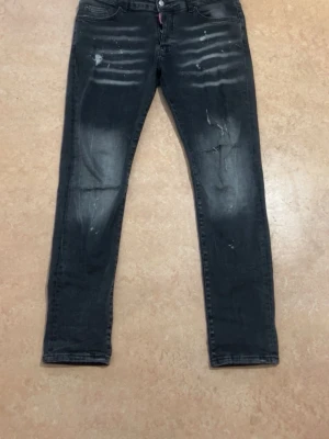Svarta skinny jeans med slitningar - Säljer ett par svarta skinny jeans med coola slitningar och blekta detaljer på låren. Jeansen har klassisk femficksdesign och knappgylf. Perfekta för en avslappnad streetstil.