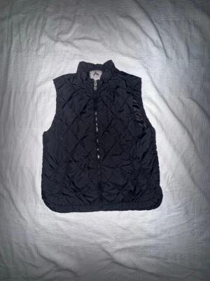 McKinley Väst - Praktisk och stilren svart väst från McKinley, perfekt för både vardag och friluftsliv. Lätt att matcha och smidig att bära som ett extra lager under kyligare dagar. Passar lika bra på promenaden som till en sportig outfit.