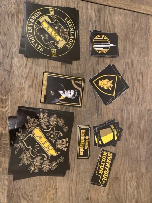 AIK klistermärken och samlarkort - Ett stort paket med AIK-klistermärken och samlarkort. Klistermärkena är svarta och gula med AIK:s logga, text som 'Svartgul kultur' och motiv från Norra Ståplats. Inkluderar även samlarkort med spelare och AIK-tema. Perfekt för AIK-supportern!               Totalt 50 stycken 