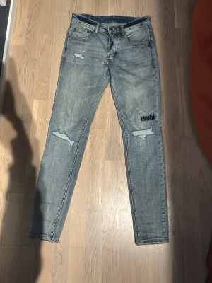 Ksubi jeans - Säljer ett par ljusblå jeans från Ksubi med slitningar och tryckdetaljer. Jeansen har smal passform, klassisk femficksdesign och coola patchar på bakfickan. Perfekta för dig som gillar streetwear och unik stil.
