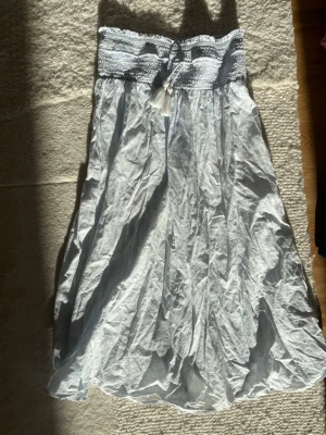 Ljusblå långkjol med smock och knyt - Långkjol i ljusblå bomull med bred smock i midjan och knytband framtill. Kjolen har ett flowy och luftigt fall, perfekt för varma dagar. Enkel att styla med crop top eller linne.