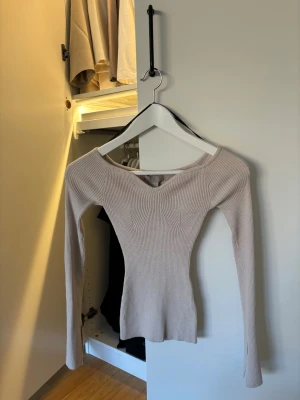 Beige ribbad långärmad topp - Säljer en beige ribbad topp med lång ärm och snygg v-ringning. Toppen har en slim passform och är tillverkad i ett stretchigt material som sitter bekvämt. Perfekt för att skapa en clean och stilren look.