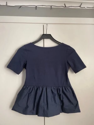 Mörkblå topp - Snygg mörkblå topp från Kappahl i storlek 158/164, toppen har en perfekt volang nertill. Toppen går ner lite i ryggen som man kan se på bild nummer 2, denna är helt oanvänd!