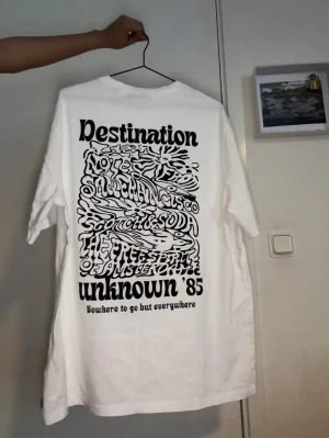 Vit oversized t-shirt med tryck - Vit oversized t-shirt från Scotch & Soda med stort grafiskt svart tryck på ryggen och mindre tryck fram. T-shirten har rund hals och korta ärmar. Perfekt för dig som gillar streetwear och vill ha en relaxed vibe.