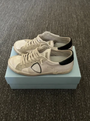 Philippe Model PRSX vita sneakers med svart detalj - Philippe Model PRSX sneakers med svart hälkappa och den ikoniska skölden på sidan. Skorna har en klassisk låg profil, vita snören och detaljer i mocka och läder. Storleken passar 42-43/5.  Skorna har tecken på användning i bland annat hälen samt på en av skornas logga, men är fortfarande omtänksamt använda samt välskötta                                                                    Hör gärna av er vid frågor!