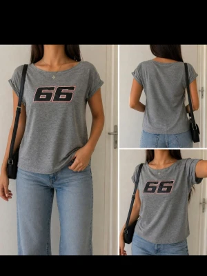 Grå t-shirt med tryck 66 - Snygg grå t-shirt med svart och rosa tryck av siffran 66 på bröstet. T-shirten har korta ärmar och rund halsringning. Perfekt till jeans för en avslappnad look.