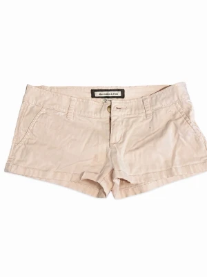 Ljusrosa shorts från Abercrombie & Fitch - Snygga beige shorts från Abercrombie & Fitch med klassisk design, fickor fram och bak samt hällor för bälte. Perfekta för varma dagar och enkla att matcha med allt. Gjorda i mjuk bomull för en skön känsla.
