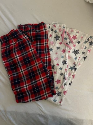 Två par pyjamasbyxor i bomull - Säljer två par mysiga pyjamasbyxor i bomull. Ena paret är röd- och blårutiga med resår i midjan, det andra är vita med rosa och svarta stjärnor samt dragsko. Perfekta för chillkvällar hemma.