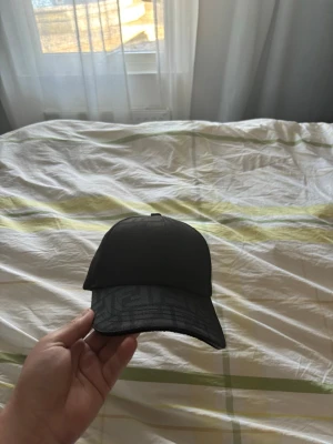 Svart keps från Fendi - Snygg svart keps från Fendi med diskret mönster på skärmen och Fendi-logga på insidan. Klassisk böjd skärm och justerbar rem baktill. Perfekt accessoar för en trendig streetwear-look.