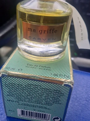 Carven Ma Griffe Eau de Parfum 50ml - Carven Ma Griffe Eau de Parfum i en elegant glasflaska med guldfärgad etikett. Parfymen kommer i en grön- och vitrandig kartong med guldiga detaljer. En klassisk och tidlös doft som passar dig som gillar exklusiva parfymer.