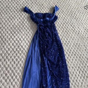 Blå glittrig bal/ fest långklänning med paljetter - Säljer en fantastisk blå långklänning med glittriga paljetter och breda axelband. Klänningen har en figurnära passform och är tillverkad i ett skimrande material med släp. Perfekt för bal eller festliga tillfällen! Klänningen är lite uppsyd så att den inte släpar för mycket