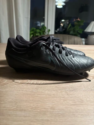 Svarta Nike tiempos - Säljer ett par svarta fotbollsskor från Nike med klassisk design och snörning. Skorna är tillverkade i läder med diskreta sömmar och har låg profil för bra bollkontroll. Perfekta för dig som vill ha stilrena och funktionella skor på planen.