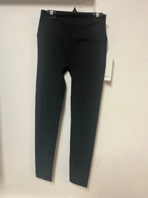 Svarta leggings från Lululemon - Snygga svarta leggings från Lululemon med hög midja och tight passform. Tillverkade i ett stretchigt och mjukt material som sitter skönt mot kroppen. Perfekta för träning eller chill. Diskret logga bak på benet.