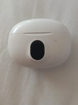Vita trådlösa hörlurar med laddningsetui - Snygga vita trådlösa hörlurar med ett ovalt laddningsetui i plast. Smidig och kompakt design som är lätt att ta med sig. Perfekt för musik, poddar och samtal på språng.