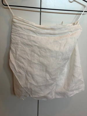 Vit linnekjol från Zara - Säljer en vit kjol från Zara i storlek M. Kjolen är tillverkad i linne och har en enkel, rak form med lätt drapering. Perfekt för dig som gillar en clean och luftig stil. Kjolen har tunna band upptill och är lätt att matcha med olika toppar.