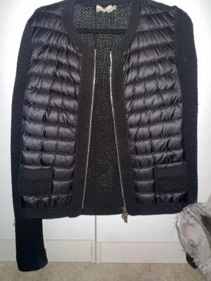 Svart cardiganjacka från Moncler - Snygg svart cardiganjacka från Moncler med quiltade partier framtill och stickade ärmar och rygg. Jackan har två fickor fram och dragkedja. Perfekt för lager-på-lager och ger en sportig men stilren look.