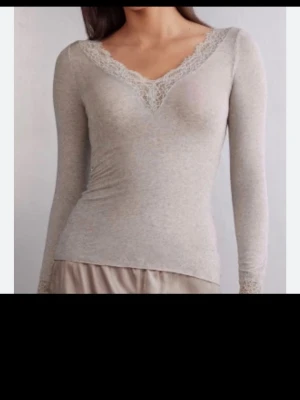 Beige långärmad topp med spets - Supersnygg beige långärmad topp med v-ringning och spetsdetaljer vid halsringningen och ärmsluten. Tunn och mjuk i materialet, perfekt att styla med jeans eller kjol. Figurnära passform som framhäver siluetten.