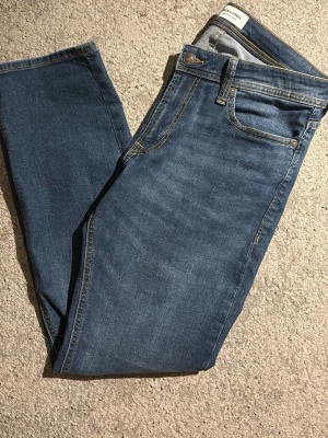 Blå jeans från Jack & Jones - Snygga blå jeans från Jack & Jones med klassisk femficksdesign och kontrastsömmar. Jeansen har rak passform och är tillverkade i ett mjukt denimtyg. Perfekta för en avslappnad och stilren look.