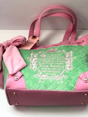 Juicy Couture daydreamer fairytale tote rosa och grön handväska - Superfin handväska från Juicy Couture i quiltad grön sammet med rosa detaljer i konstläder. Väskan har dubbla handtag, dekorativ rosett och broderad logga framtill. Guldiga metalldetaljer och snörning upptill ger extra stilpoäng.