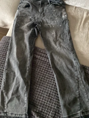 Grå raka jeans med pärldetaljer - Säljer ett par grå jeans med raka ben och coola vita pärldetaljer framtill. Jeansen har klassisk femficksmodell och hög midja. Materialet är denim i bomull och de har en avslappnad passform som passar perfekt till en trendig streetstyle-look.