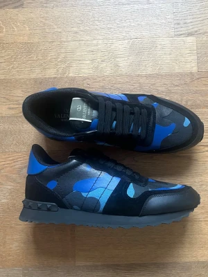 Valentino rockrunners   - Snygga sneakers från Valentino med blå och svart camo-mönster. Skorna har svarta skosnören, detaljer i läder och textil samt nitar på hälen. Perfekt för dig som vill sticka ut med ett coolt och unikt par sneakers. Nytt skick
