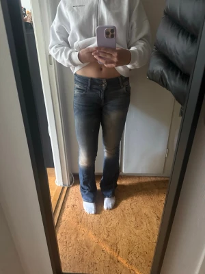 Blå bootcut jeans med slitningar - Säljer ett par blå bootcut jeans med snygga slitningar och tvättade detaljer på låren och knäna. Jeansen har klassisk femficksmodell och normal midja. Perfekta för en avslappnad och trendig look.