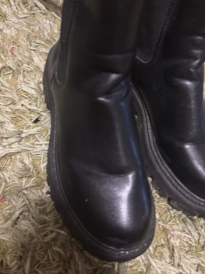 Svarta chunky läderstövlar - Säljer ett par svarta stövlar i slätt läder med chunky sula. Klassisk modell med rund tå och diskreta sömmar längs skaftet. Perfekta för dig som gillar en stilren och edgy look till hösten eller vintern.