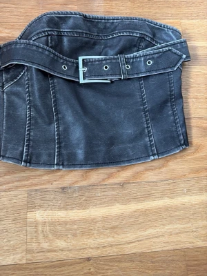 Svart denimkorsett med bälte SOYA - Cool svart korsett i denim från SOYA med markerade sömmar och tillhörande bälte med metallspänne. Dragkedja bak för enkel påklädning. Perfekt för att skapa en edgy look.