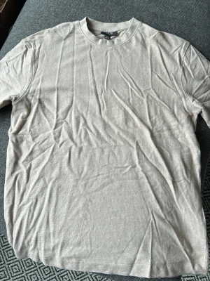 Beige t-shirt från SMOG relaxed fit - En stilren beige t-shirt från SMOG i relaxed fit. T-shirten är kortärmad och tillverkad i mjuk bomull, perfekt för en chill och enkel look. Passar dig som gillar basic plagg med skön passform.