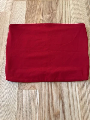 Röd bandeau tubtopp - En enkel och stilren röd bandeau tubtopp i mjukt material. Perfekt att matcha med höga jeans eller kjol för en trendig look. Toppen är ärmlös och har en tight passform som sitter snyggt på kroppen.