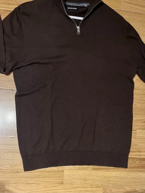Brun stickad tröja Jack & Jones - Mörkbrun stickad tröja från Jack & Jones med half zip-dragkedja i halsen. Tröjan har ribbade muddar vid ärmslut och nederkant, perfekt för en clean och stilren look. Passar dig som gillar klassiska plagg med modern touch. Mvh✌️