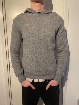 Oscar Jacobson hoodie - Säljer en stilren grå hoodie i kashmir från Oscar Jacobson. Hoodien har en klassisk huva, ribbade muddar vid ärmslut och nederkant samt en enkel, clean look utan tryck eller dragkedja. Perfekt för dig som gillar minimalistisk stil.