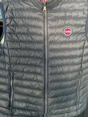 Mörkblå dunväst från Colmar - Snygg mörkblå dunväst från Colmar med quiltad design och dragkedja framtill. Västen har två fickor med dragkedja och ett broderat Colmar-märke på bröstet. Perfekt för lager-på-lager och riktigt skön att bära under kyliga dagar.