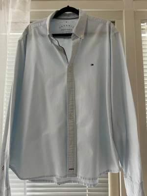 Ljusblå Oxfordskjorta Tommy Hilfiger - Klassisk ljusblå Oxfordskjorta från Tommy Hilfiger i ekologisk bomull. Skjortan har lång ärm, knappar framtill och den ikoniska lilla loggan broderad på bröstet. Perfekt för en clean och stilren look. Priset kan diskuteras vid snabb affär 