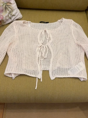 Vit virkad kofta från Xside - Säljer en vit, virkad kofta från Xside med knytband framtill. Koftan har ett luftigt nätmönster, trekvartsärmar och är croppad i modellen. Perfekt att slänga över ett linne eller klänning för en avslappnad look. Den är dock liten i storlek så den skulle passa folk som bär S/Xs!!  Inte använd en enda gång. 
