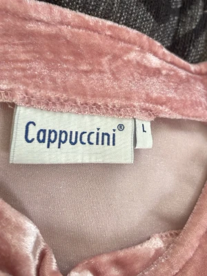 Rosa sammets t-shirt från Cappuccini - Superfin rosa t-shirt i sammetsmaterial från Cappuccini. T-shirten har korta ärmar och en mjuk, glansig yta som ger en lyxig känsla. Perfekt för dig som vill sticka ut med en unik topp i garderoben.