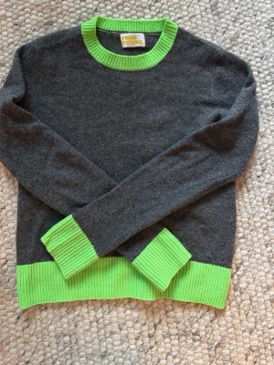 From Future tröja - Stickad tröja från From Future i mörkgrått med ribbade neongröna detaljer vid hals, ärmslut och nederkant. Tillverkad i 100% cashmere för en mjuk och lyxig känsla. I jättebra skick förutom ett litet lagat hål på höger underarm(igen sytt). Priset går att förhandla vid snabb affär💕 Med kommer oxkså en from future totebag vid köp 
