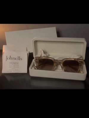 Chimi solglasögon i beige och guld - Snygga solglasögon från Chimi med transparent beige båge och gulddetaljer. Glasen är lätt tonade i brunt och har en fyrkantig form som ger en trendig look. Kommer i original förpackning med allt kvar- påse putsduk kvitto kartong. Väl om händertagna solgalsögon. Skicka gärna frågor och prisförslag svarar fort 