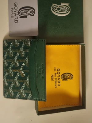 Grön korthållare från G4yard - Snygg grön korthållare från G4yard med det klassiska vita och gröna mönstret. Tillverkad i exklusivt läder och canvas, har flera fack för kort och detaljer i guldtext. Kommer med original ask och putsduk.